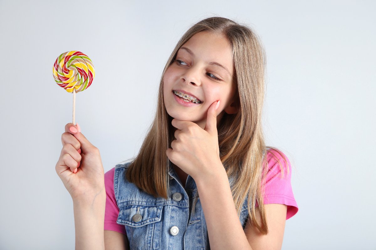 How Chewy Candy Affects Your Braces Young girl holding colorful lollipop, smiling thoughtfully against white background.