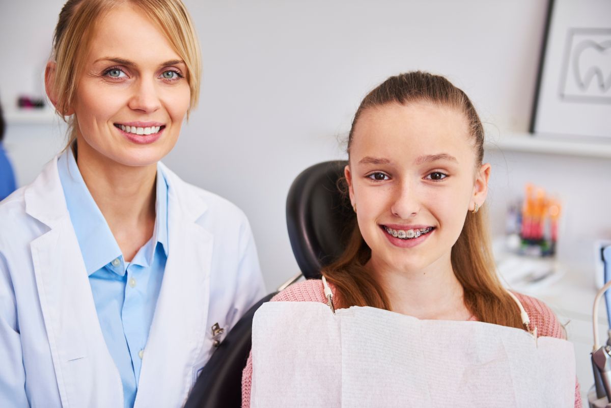 Smiling,Female,Orthodontist,And,Child,In,Dentist’s,Office Female orthodontist with young patient holding dental X-ray in modern office setting.