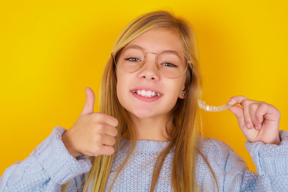Smiling young woman giving thumbs up against yellow background, showcasing confident smile.