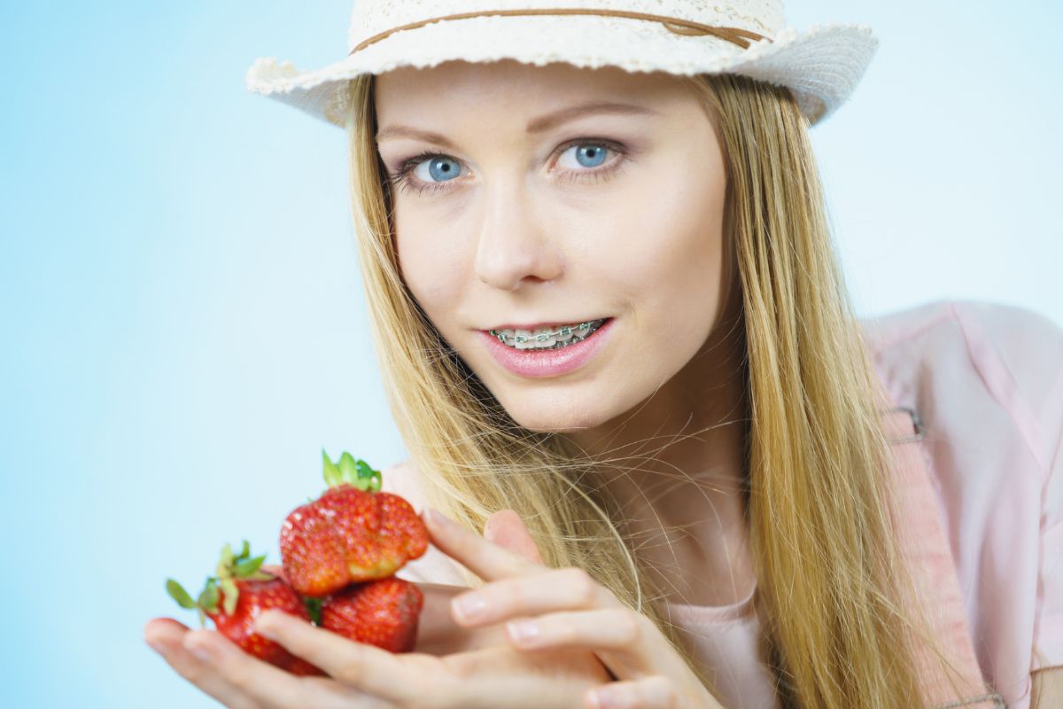 Young woman in straw hat holding fresh strawberries against blue background